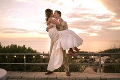 a bride and groom kissing in front of the sunset