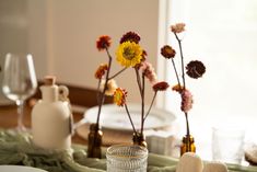 the table is set with dishes and vases filled with wildflowers in glass bottles