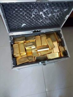 an open briefcase filled with gold bars on top of a tile floor in a room