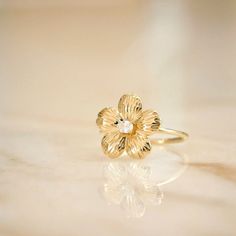 The Cherry Blossom Ring is your new forever flower. Designed with an etched effect adorning each petal surrounding a central oval diamond, this sweet ring is one of nature’s finest. Gold Rings Flower Design, Flower Gold Rings, Anniversary Flower Ring With Center Stone, Delicate Flower Ring With Rose Cut Diamonds, Dainty Oval Yellow Gold Flower Ring, Flower Shaped Promise Ring With Rose Cut Diamonds, Delicate 14k Gold Flower Ring With Rose Cut Diamonds, Yellow Gold Diamond Flower Ring For Proposal, Elegant Yellow Gold Engraved Ring With Birth Flower