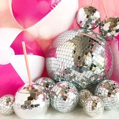 shiny disco balls and straws in front of a pink wall with white and silver balloons