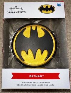 the batman ornament in its box is yellow and has a bat symbol on it