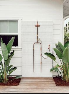 a white house with some plants in front of it and a water spigot on the wall