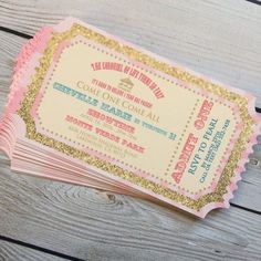 some pink and gold tickets are stacked on top of each other in front of a wooden table