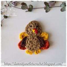 a small crocheted turkey sitting on top of a white table next to leaves