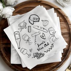 four napkins on a wooden plate with white flowers and wine glasses in the background