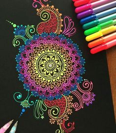 colored pencils are next to a drawing of a colorful flower on a black paper