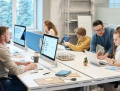 a group of people sitting around a table working on laptops and tablets in front of them