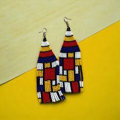 These beautiful Mondrian style beaded earrings are a perfect finishing touch to any outfit and make a statement. The intricate woven pattern in black, yellow, red, blue and white emphasizes the artistic beauty of this piece.  Wear them with a simple white blouse or combine them with an ethnic ensemble for a boho-chic look. Give them as a statement piece or keep them all to yourself - either way, these earrings are sure to turn heads. They are made with a lot of passion and love by Colombian hand Elegant Multicolor Handmade Beaded Earrings, Artsy Colorful Beaded Earrings As Gift, Unique Multicolor Handwoven Earrings, Unique Handwoven Multicolor Earrings, Multicolor Woven Drop Earrings, Multicolor Woven Beaded Dangle Earrings, Traditional Multicolor Woven Earrings, Traditional Woven Multicolor Earrings, Simple White Blouse