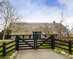 a house with a thatched roof next to a wooden gate and brick walkway in front of it