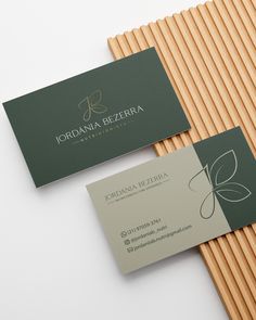 two business cards sitting next to each other on top of a white surface with wood slats