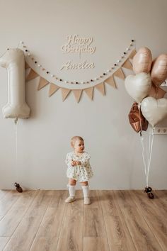 a baby girl standing in front of balloons and streamers with the words happy birthday printed on it