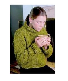 a woman wearing a green sweater is holding a cup