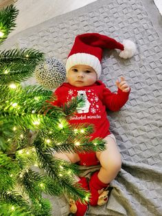 a baby laying on top of a blanket next to a christmas tree with a santa hat