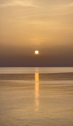 the sun is setting over the ocean with calm water