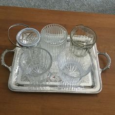 an assortment of glassware on a tray with silver trimmings sitting on a wooden table