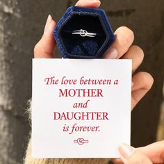 a person holding up a card with a ring on it that says, the love between a mother and daughter is forever