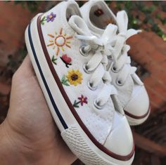 someone is holding their white shoes with embroidered flowers on them