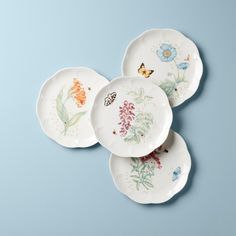 three plates with different designs on them sitting on a blue surface, one has a butterfly and the other has flowers