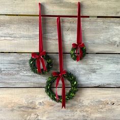 two christmas wreaths hanging on the side of a wooden wall with red ribbon and bows