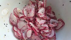 sliced radishes in a white bowl with black seeds and seasoning on top