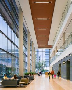 people are walking through the lobby of an office building with high ceilings and large windows