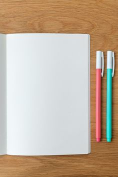 two pens sitting on top of an open notebook next to another pen and eraser