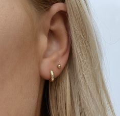 a close up of a woman's ear wearing a pair of tiny gold hoop earrings