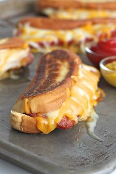 two hot dogs with cheese and ketchup on a tray next to some dipping sauces