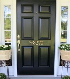 the front door is painted black and has two planters on either side