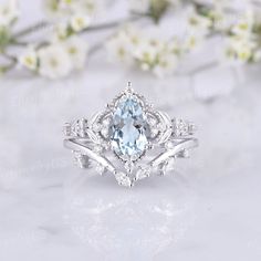 an oval blue topazte surrounded by smaller white diamonds sits on a marble surface with flowers in the background