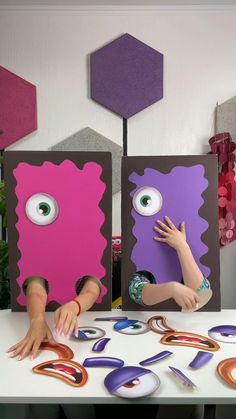 two children are playing with paper cutouts and making monster faces on the table in front of them