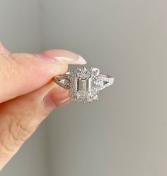 a woman's hand holding a ring with an emerald stone and diamond accents on it