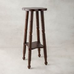 a small wooden stool with two legs and a seat on the bottom, sitting in front of a white wall