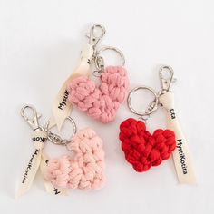 three knitted heart shaped keychains are shown on a white surface, one is red and the other is pink