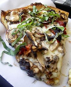 a slice of mushroom pizza sitting on top of a white paper plate covered in greens