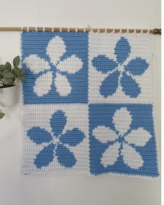 a blue and white crocheted wall hanging next to a potted green plant