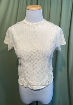 "This is a sweet vintage, lace blouse from the 1950s or 60s. Label is missing, no size tag, the bust measures 32\", but would look best on a slightly smaller bust. Please see measurements below. Made of a rayon or nylon eyelet layer over a silky solid layer in an off white or cream color. Button back , with plastic buttons. The neckline is high & rounded. Hem line is a straight hemline, with small vents over each hip. The blouse is in very good condition! No damage , but it does have a tiny Fitted Retro Cream Top, Cream Fitted Top With Lace Collar, Fitted Cream Top With Lace Collar, Fitted Vintage White Top With Lace Trim, Vintage Lace Top In Vintage White, Fitted Cream Lace Top With Short Sleeves, Vintage White Fitted Retro Top, Fitted Tops With Lace Collar For Vintage Fashion, Vintage Lace Tops For Spring