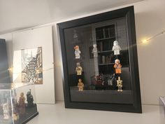 some legos are in a black frame on a white shelf and there is a glass case that holds them