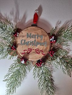 a merry christmas sign hanging from the side of a wooden plaque with pine branches and berries