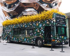 a bus covered in green and yellow flowers parked on the side of the road next to a building