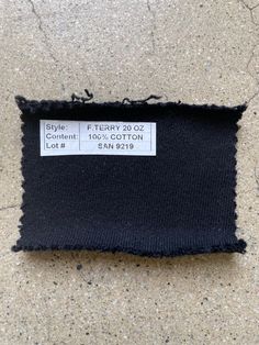 black fabric with white stitching on the bottom and one side is torn off to reveal a price label