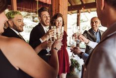 a group of people standing around each other holding wine glasses in their hands and laughing