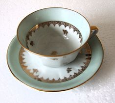 two tea cups and saucers sitting side by side on top of each other with gold trimmings