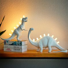 two white dinosaur figurines sitting on top of a wooden shelf next to a plant