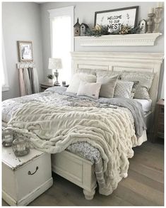 a white bed sitting in a bedroom next to a window with lots of pillows and blankets on top of it