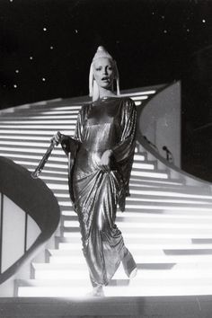 the woman is walking down the stairs with her hand on her hip while wearing a shiny dress