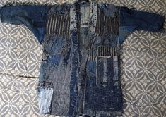 an old blue jean jacket is laying on top of a patterned bed sheet, with holes in the fabric