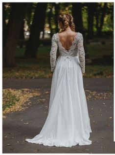 the back of a woman's wedding dress as she walks down a path in front of trees