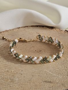 a bracelet with green and white beads on a piece of wood next to a white cloth